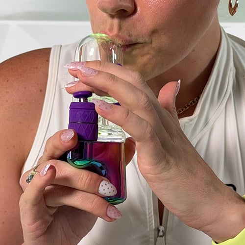 Woman inhaling from Bomb Aerix Erig with the glass mouthpiece