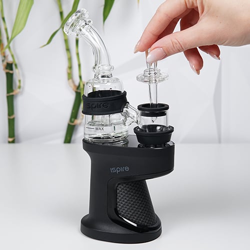 Ispure Daab Kit on a table while woman is holding a glass carb cap near heating chamber