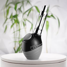 Une batterie Lookah Egg à filetage 510 posée sur une surface circulaire blanche avec un fond flou de plante verte.