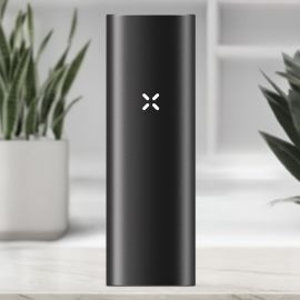 Front view of the PAX Mini vaporizer in Onyx colour, featuring the illuminated PAX logo on the sleek black aluminium body, placed on a modern indoor background.